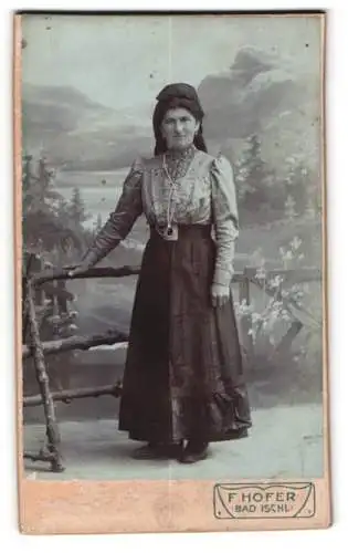 Fotografie Franz Hofer, Bad Ischl, Stehende Frau in Tracht vor malerischer Kulisse
