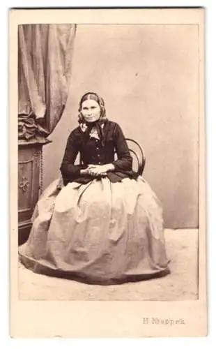 Fotografie Heinrich Krappek, Ort unbekannt, sitzende Dame mit Kopfbedeckung, Reifrockkleid