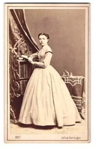 Fotografie Julius Gertinger, Wien, Margarethenstrasse 28, Dame in elegantem Kleid lehnt am Bücherregal