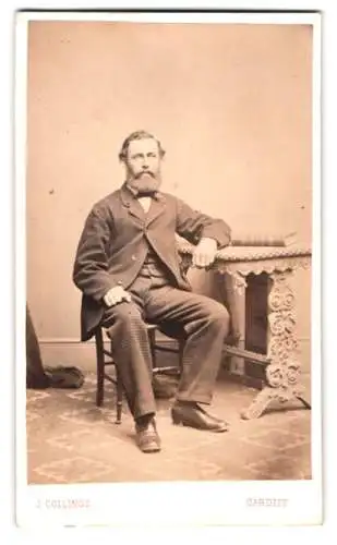 Fotografie J. Collings, Cardiff, Bute Street 47, waliser Herr auf elegantem Stuhl neben verziertem Tisch