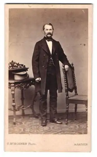 Fotografie C. Schoenen, Aachen, Damengraben 16, Herr im Anzug stehend vor Tisch mit Zylinder