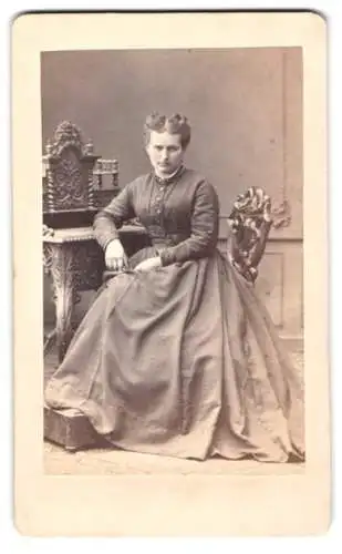Fotografie August Linde, Gotha, Auguststrasse 3, Dame in elegantem Kleid an reich verziertem Möbelstück