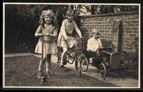 Foto-AK Zwei Mädchen auf Roller und Fahrrad, Junge im Spielzeugauto, Garten