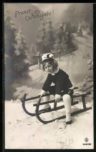 AK Kind auf einem Schlitten vor Winterstudiokulisse, Prosit Neujahr