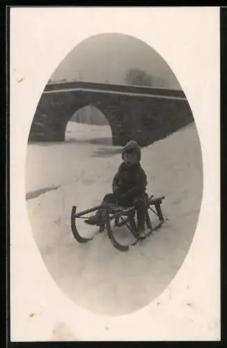 Foto-AK Kind auf einem Schlitten vor einer Brücke