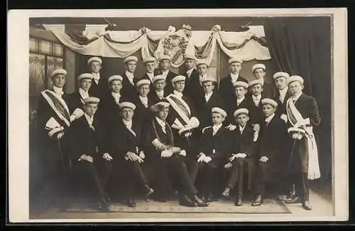 Foto-AK Studenten mit Mützen, Degen und Wappen unter einer gerüschten Fahne, Gruppenfoto