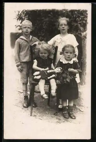Foto-AK Porträt von vier Kindern, ein Mädchen hat eine Puppe auf dem Schoss
