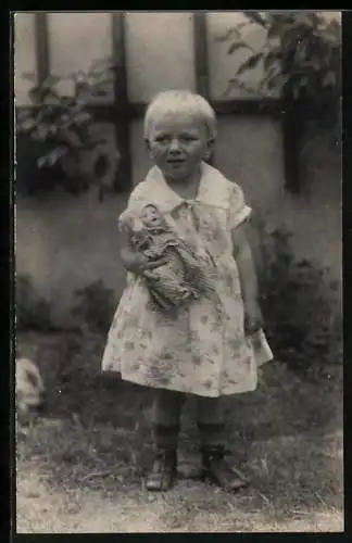 Foto-AK Mädchen in einem geblümten Kleid hält eine Puppe in den Armen, Sommer 1928