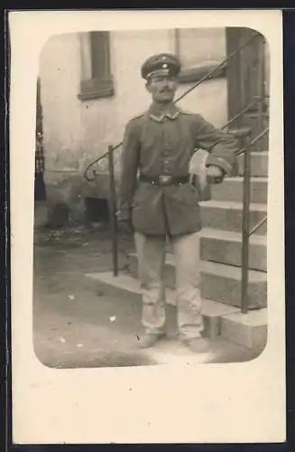 Foto-AK Soldat mit Schirmmütze vor einem Hauseingang, Uniformfoto
