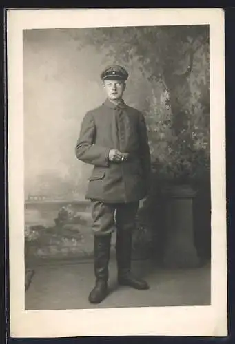 Foto-AK Soldat mit Schirmmütze u. Zigarette vor Fotokulisse, Uniformfoto