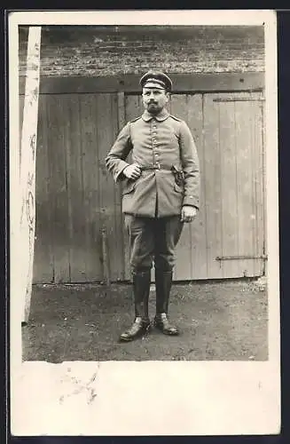 Foto-AK Soldat mit Schirmmütze u. Pistolentasche vor einem Garagentor, Uniformfoto