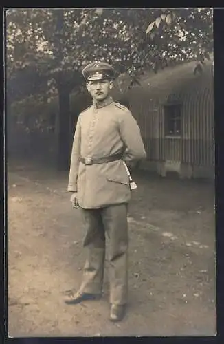 Foto-AK Soldat mit Schirmmütze u. Quaste vor einer Baracke, Uniformfoto