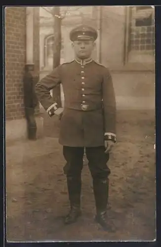 Foto-AK Soldat mit Schirmmütze und Kragenspiegel vor einem Gebäude, Uniformfoto