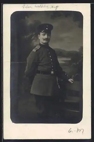 Foto-AK Soldat mit Schirmmütze u. Schulterabzeichen vor Fotokulisse, Uniformfoto