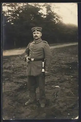 Foto-AK Soldat mit Quaste auf einem Feld, Uniformfoto