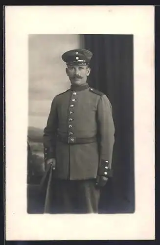 Foto-AK Soldat mit Schirmmütze vor Fotokulisse, Uniformfoto