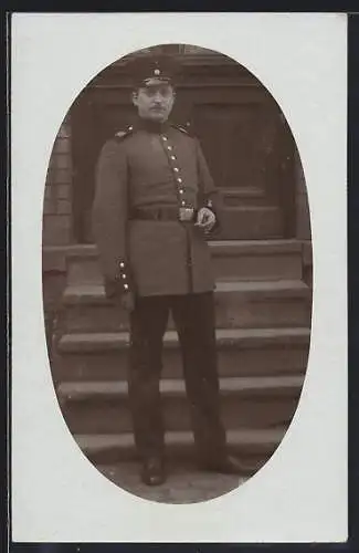 Foto-AK Soldat mit Schirmmütze vor einer Treppe, Uniformfoto