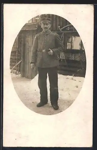 Foto-AK Soldat mit Schirmmütze im Schnee vor einem Gebäude, Uniformfoto