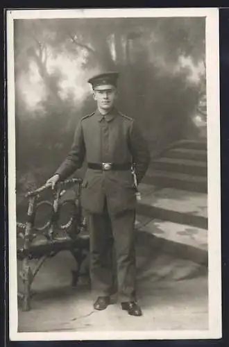 AK Soldat mit Schirmmütze und Quaste vor Fotokulisse, Uniformfoto