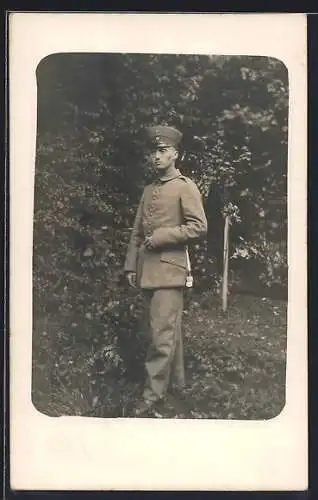 Foto-AK Soldat mit Schirmmütze und Quaste in einem Garten, Uniformfoto