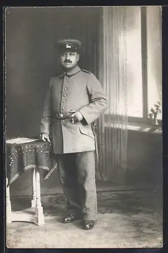 Foto-AK Soldat mit Schirmmütze u. Zigarre in einer Stube, Uniformfoto