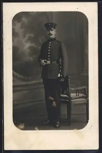 Foto-AK Soldat mit Schirmmütze u. Quaste in einer Stube, Uniformfoto