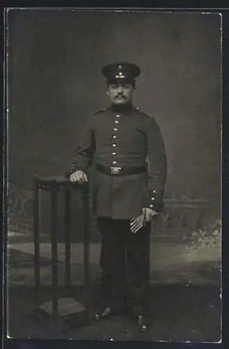 Foto-AK Soldat mit Schirmmütze u. Handschuhen vor einer Fotokulisse, Uniformfoto