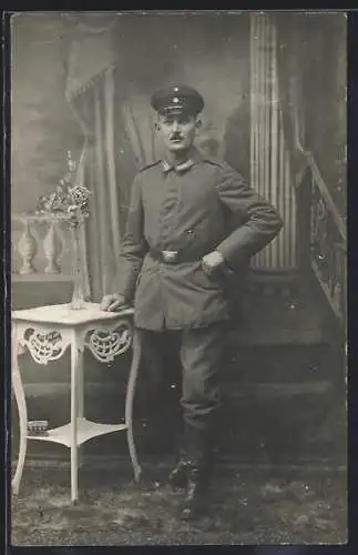 Foto-AK Soldat mit Schirmmütze u. Kragenspiegel vor einer Fotokulisse, Uniformfoto
