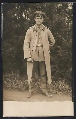 Foto-AK Soldat im Mantel in einem Garten, Uniformfoto