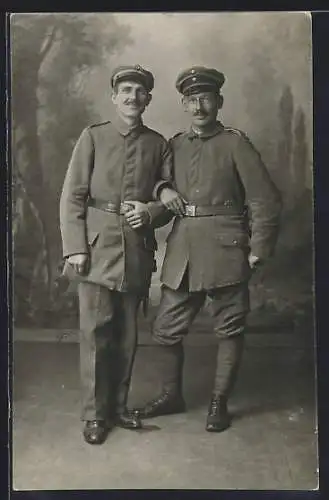 Foto-AK Zwei Soldaten mit Schirmmützen vor Fotokulisse, Wickelgamaschen, Uniformfoto