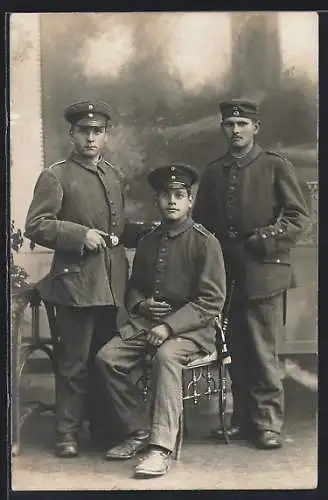 Foto-AK Drei Soldaten mit Schirmmützen u. Quaste vor Fotokulisse, Uniformfoto