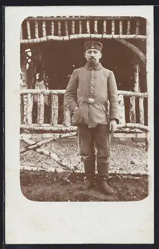 Foto-AK Soldat mit Degen vor einem Lattengebilde, Uniformfoto