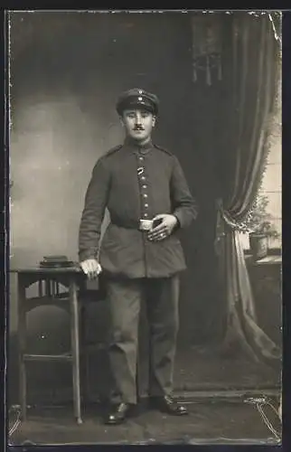 Foto-AK Soldat mit Schirmmütze vor einer Fotokulisse, Uniformfoto