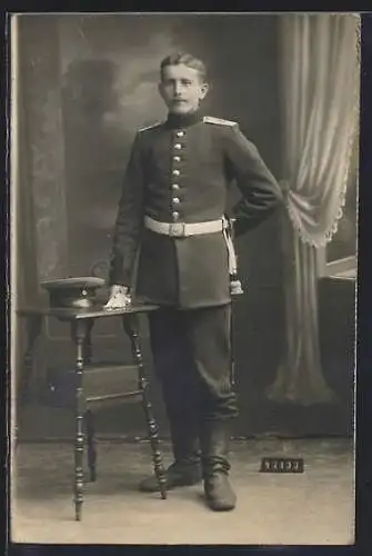 Foto-AK Soldat mit Schirmmütze und Quaste vor einer Fotokulisse, Uniformfoto