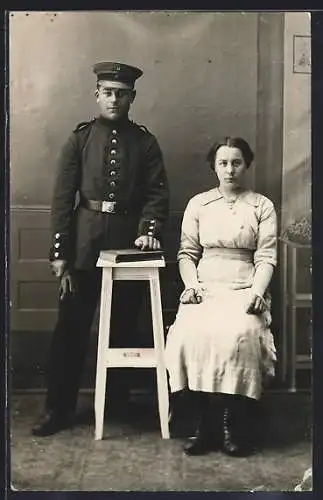 Foto-AK Soldat mit Schirmmütze und junge Frau vor einer Fotokulisse, Uniformfoto