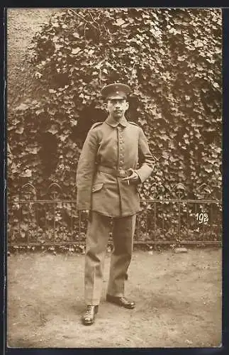Foto-AK Soldat mit Schirmmütze und Zigarette in einem Garten, Uniformfoto