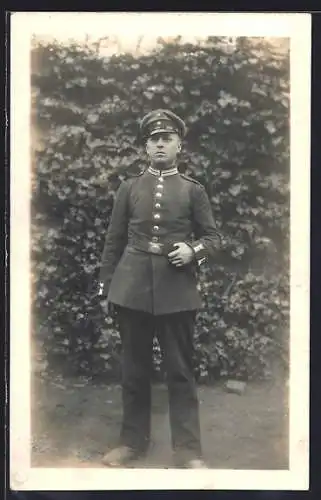 Foto-AK Soldat mit Schirmmütze und Kragenspiegel in einem Garten, Uniformfoto