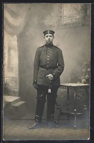 Foto-AK Soldat mit Quaste u. Degen vor Fotokulisse, Uniformfoto