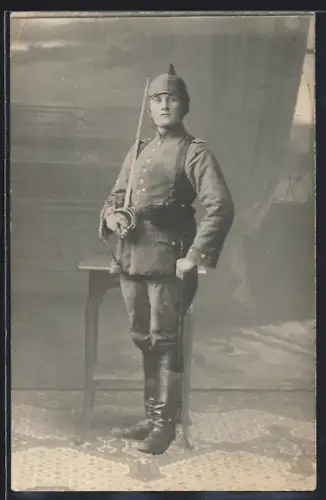 Foto-AK Soldat in Feldgrau Uniform mit Säbel, Magazintaschen und Pickelhaube