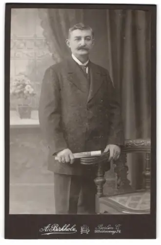 Fotografie A. Birkholz, Berlin, Weidenweg 34, Herr mit gerolltem Dokument