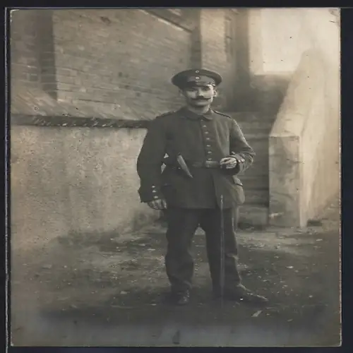 Foto-AK Soldat in Feldgrau Uniform mit Pistolentasche und Schirmmütze