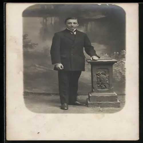 Foto-AK Eleganter Herr an Säule in einer Studiokulisse