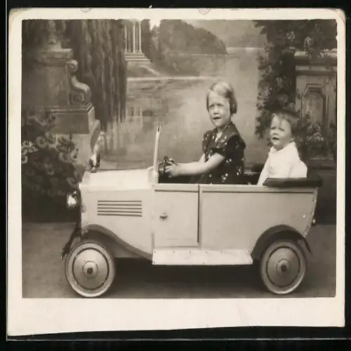 Fotografie Spielzeug-Auto, Mädchen und Knabe im Tretauto mit Kühlerfigur Indianer-Häuptling