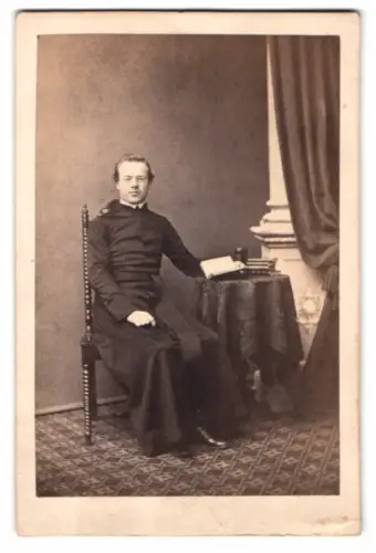 Fotografie N. A. Dietz, München, Pastor im Talar posiert sitzend im Atelier