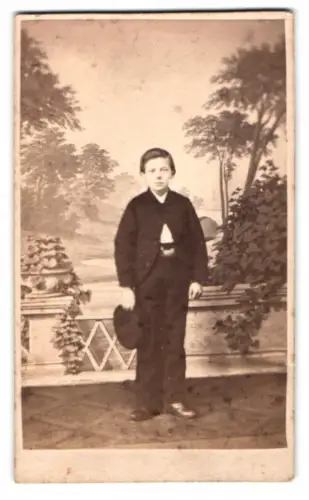 Fotografie unbekannter Fotograf und Ort, junger Knabe in Anzug mit Hut vor einer Studiokulisse