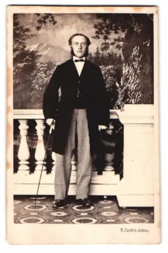 Fotografie N. Smith, Göteborg, Östra Hamngatan 18, Porträt eines eleganten Herrn im Anzug mit Zylinder und Flanierstock