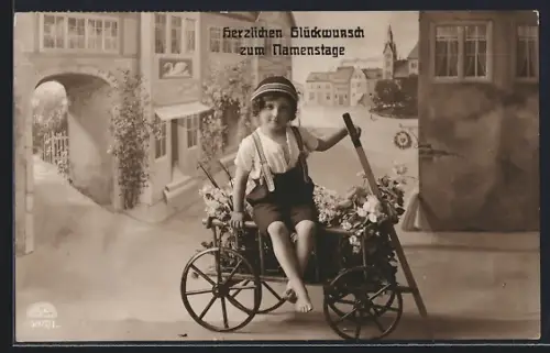 Foto-AK R & K / L Nr. 5697/1: Kleiner Gratulant mit Blumenwagen vor Strassenkulisse, Namenstagsgruss