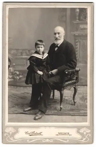 Fotografie Carl Gründl, Villach, Klagenfurterstrasse 5, Porträt eines älteren Mannes mit Kind auf dem Schoss, 1905