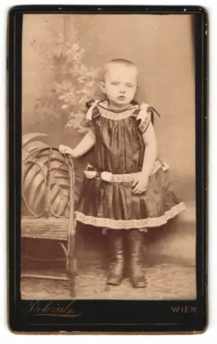 Fotografie A. Müller, Wien, Neubaugasse 31, Kleinkind in Kleid neben Stuhl