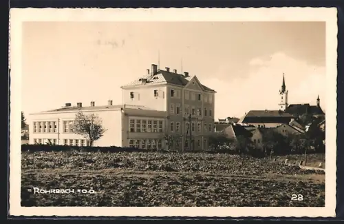 AK Rohrbach /O.-Ö., Ortspanorama mit grossem Gebäude und Kirchturm von einem Feld aus